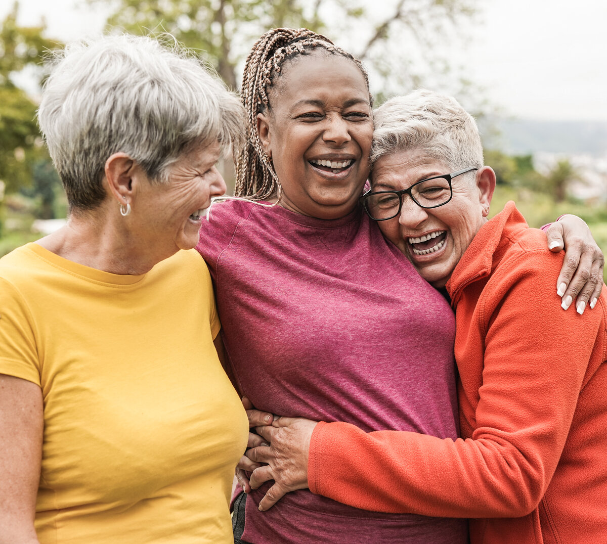 Happy multiracial senior women having fun together outdoor - Elderly generation people hugging each other at park